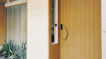 A building entrance with a wooden door, a mailbox, and a wall with a number sequence.