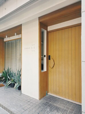 A building entrance with a wooden door, a mailbox, and a wall with a number sequence. - Baan Rak (Bangkok)