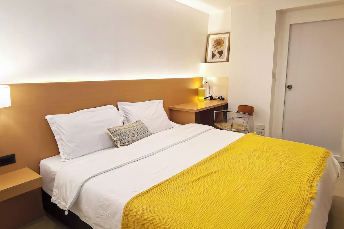 A hotel room with a bed, bedside table, lamp, and a framed picture on the wall.
