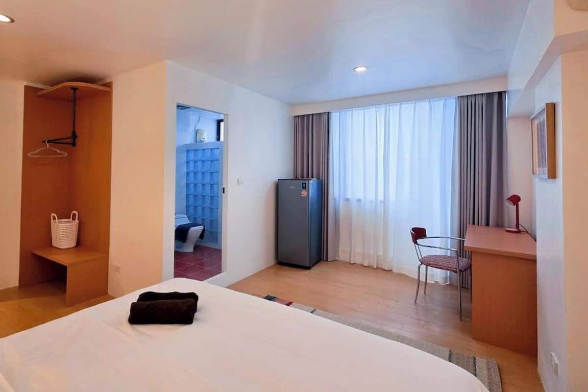 A hotel room with a bed, a desk, a chair, a refrigerator, and a bathroom visible through an open door.