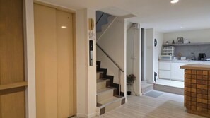 A modern kitchen with a wooden counter, a staircase with a handrail, and a door leading to another room. - Baan Rak (Bangkok)