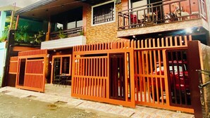 A two-story building with a balcony on the upper floor, a gated entrance, and a visible car parked inside. - Lens Staycation Serene 2-BDR-1BR-KTCHN-Wifihouse with AC in peaceful Panabo (Panabo)