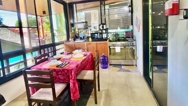 A dining area with a table set for two, a ceiling fan, and a kitchen area visible through a glass partition. - Lens Staycation Serene 2-BDR-1BR-KTCHN-Wifihouse with AC in peaceful Panabo (Panabo)