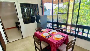 A dining area with a table set for four, a ceiling fan, and a view through large windows. - Lens Staycation Serene 2-BDR-1BR-KTCHN-Wifihouse with AC in peaceful Panabo (Panabo)