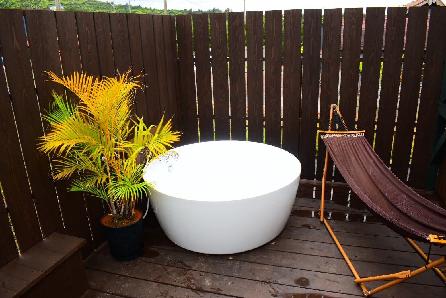 A wooden deck with a white hot tub, a hammock, and a potted plant.