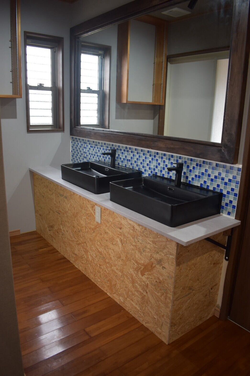 A kitchen with a wooden countertop, three black sinks, and a tiled backsplash.