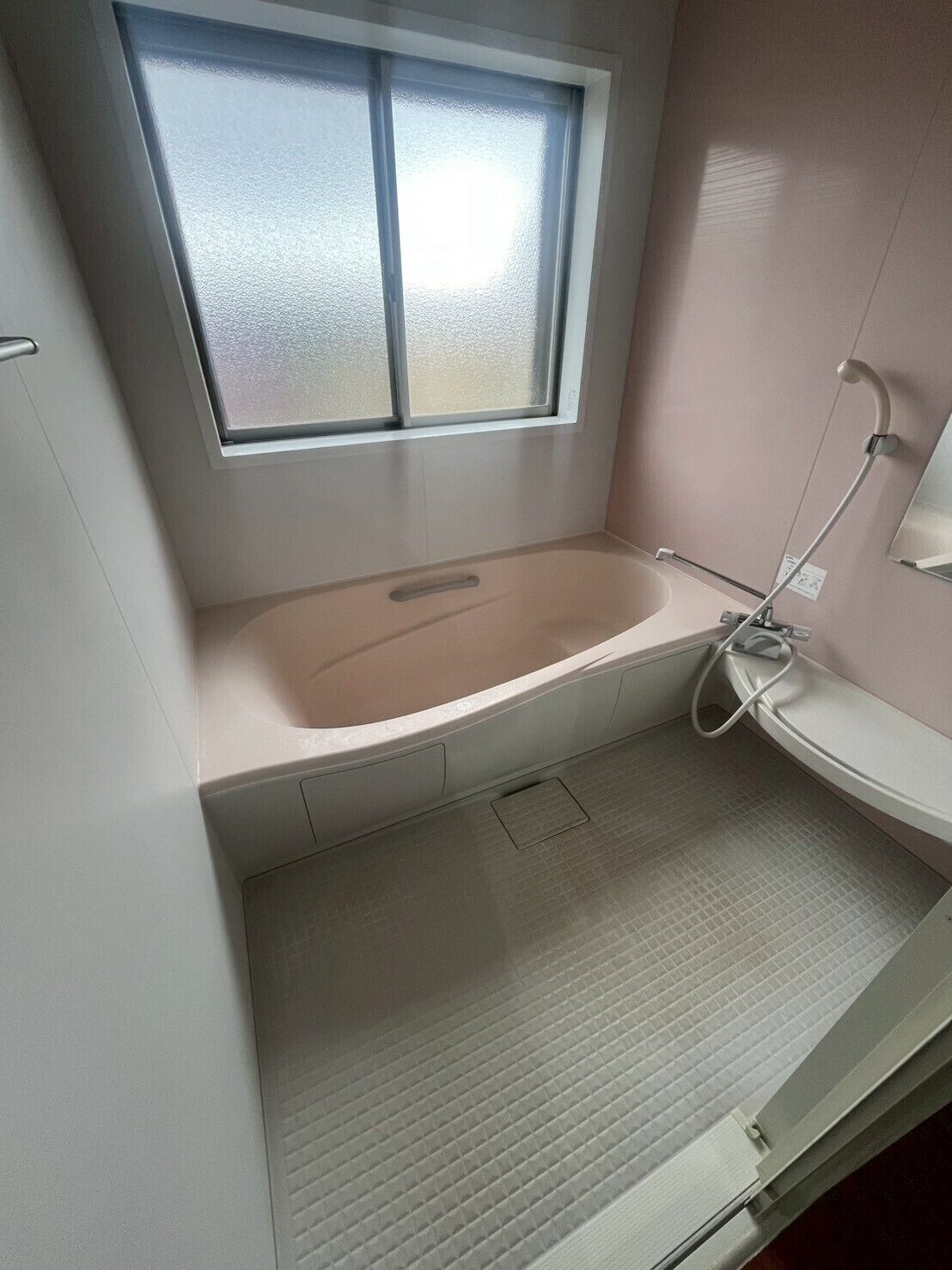 A small bathroom with a bathtub, a window, and a shower.
