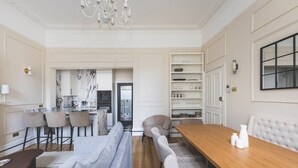 A modern dining area with a wooden table, cushioned benches, and a chandelier. - Elegant South Kensington Retreat (London)
