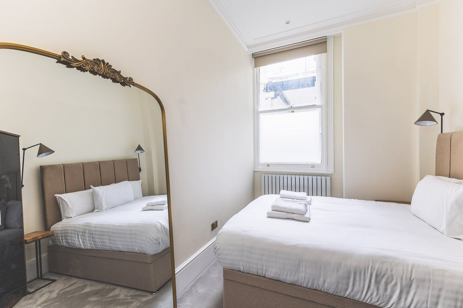 Una habitación de hotel con cama, mesita de noche, lámpara, ventana y radiador.