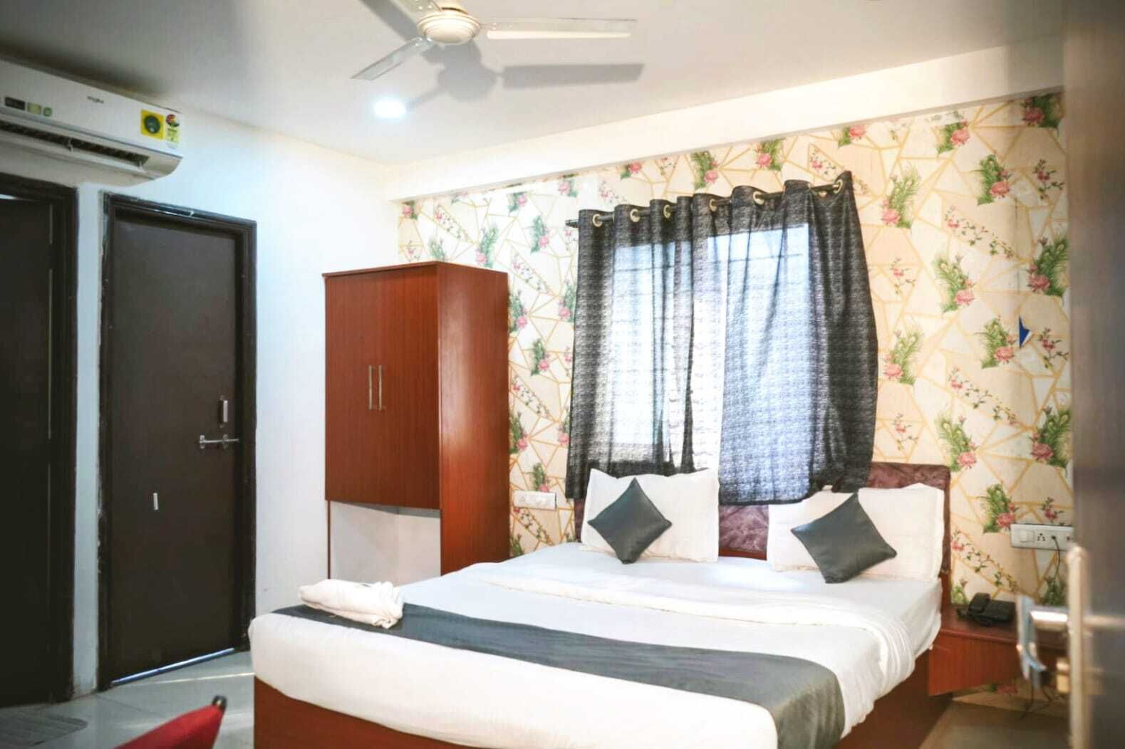 A hotel room with a bed, a wardrobe, a ceiling fan, and floral wallpaper.