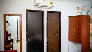 A room with two dark wooden doors, a wardrobe, a tripod, and an air conditioning unit. - Hotel The Cozy Stay (Indore)