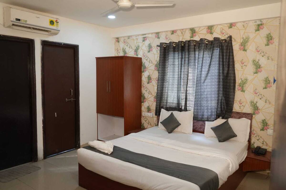 A bedroom with a bed, curtains, a wardrobe, and an air conditioning unit.