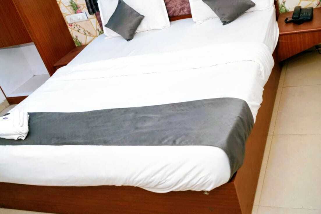 Una cama bien hecha con ropa de cama blanca y gris, un cabecero de madera y una mesita de noche con un teléfono.