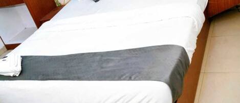 Una cama bien hecha con ropa de cama blanca y gris, un cabecero de madera y una mesita de noche con un teléfono.
