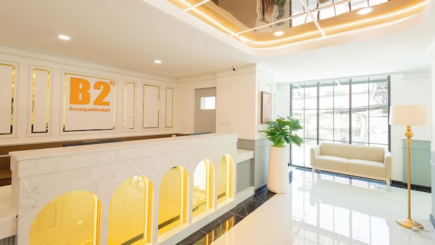 A modern hotel lobby with a reception desk, a sofa, a potted plant, and a large window. - B2 Future Park Rangsit Boutique & Budget (Thanyaburi)