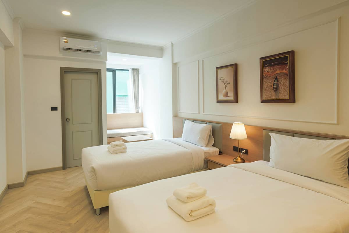 A hotel room with two beds, a TV, an air conditioning unit, and a window with curtains.
