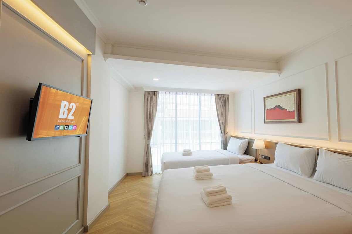 A hotel room with two beds, a TV, a painting, and a window with curtains.