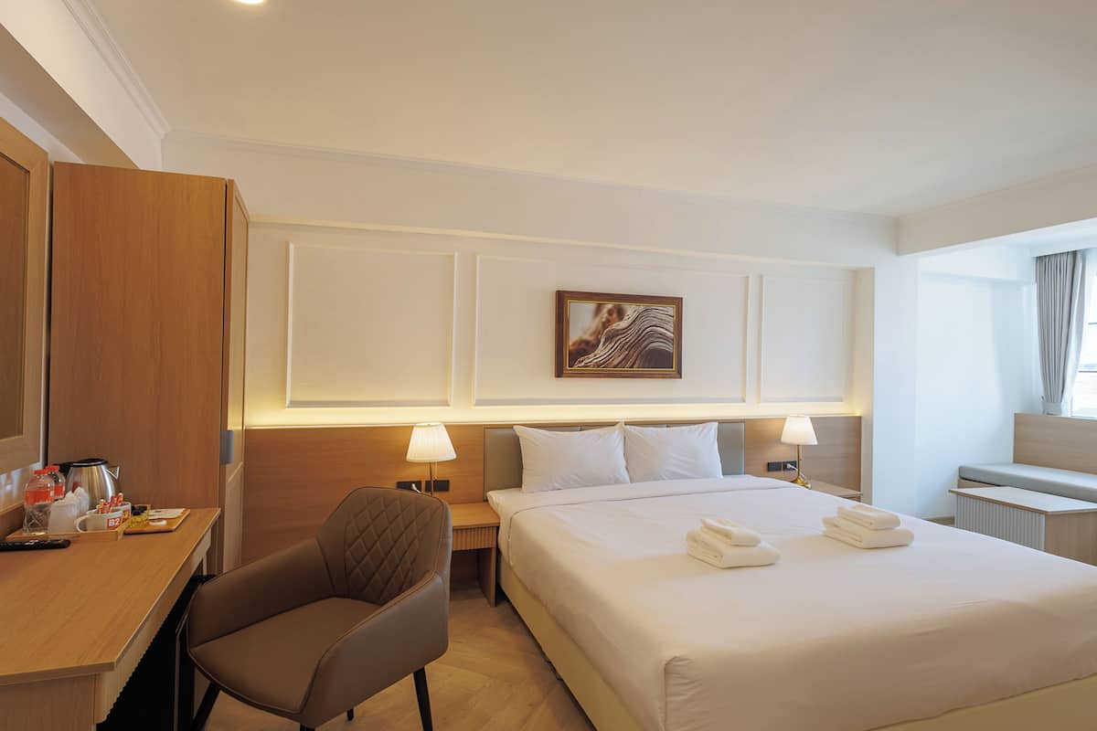 A hotel room with a bed, a desk, a chair, a nightstand, and a large mirror.