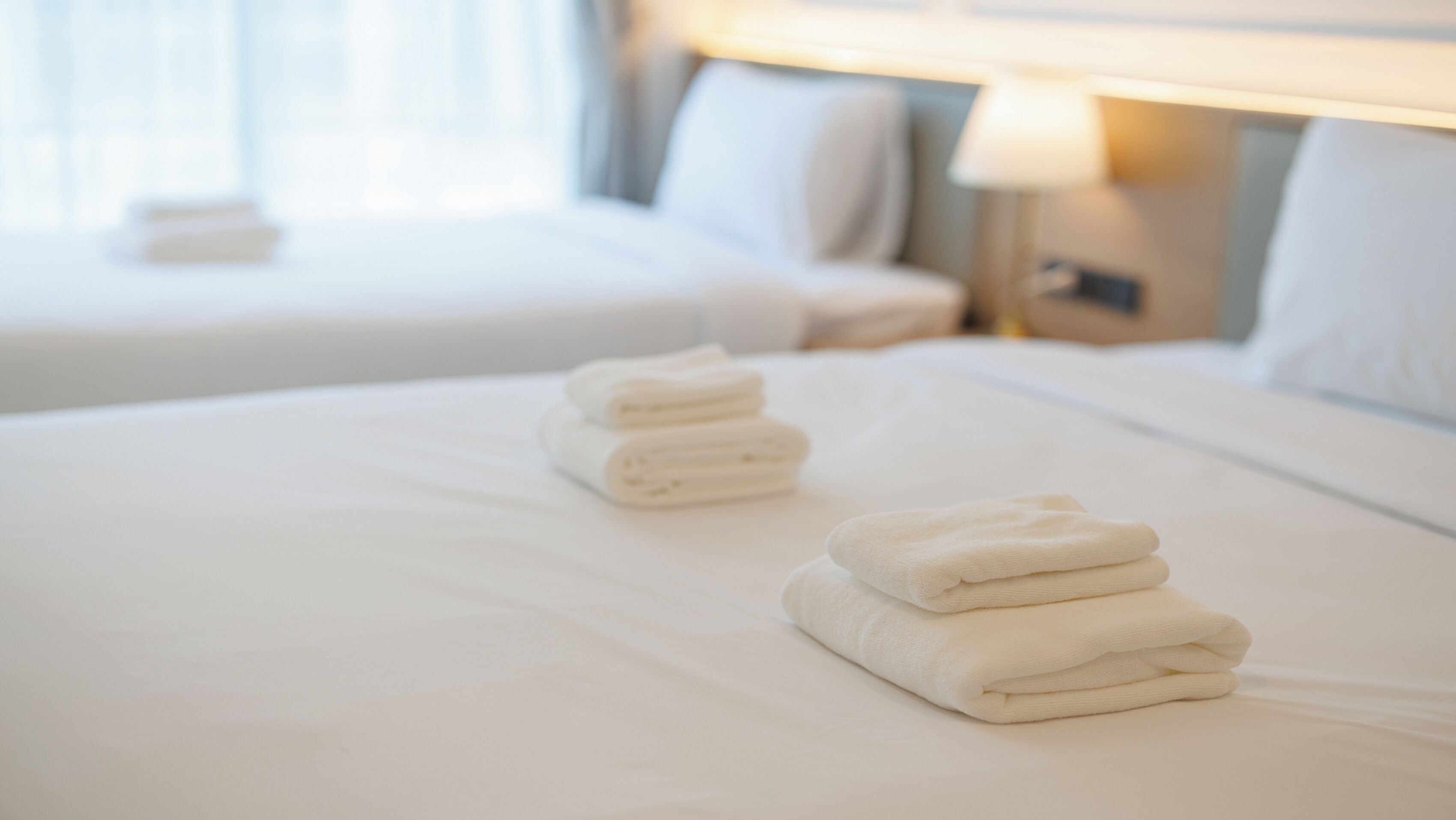 A hotel room with a neatly made bed, a nightstand with a lamp, and a window with curtains.