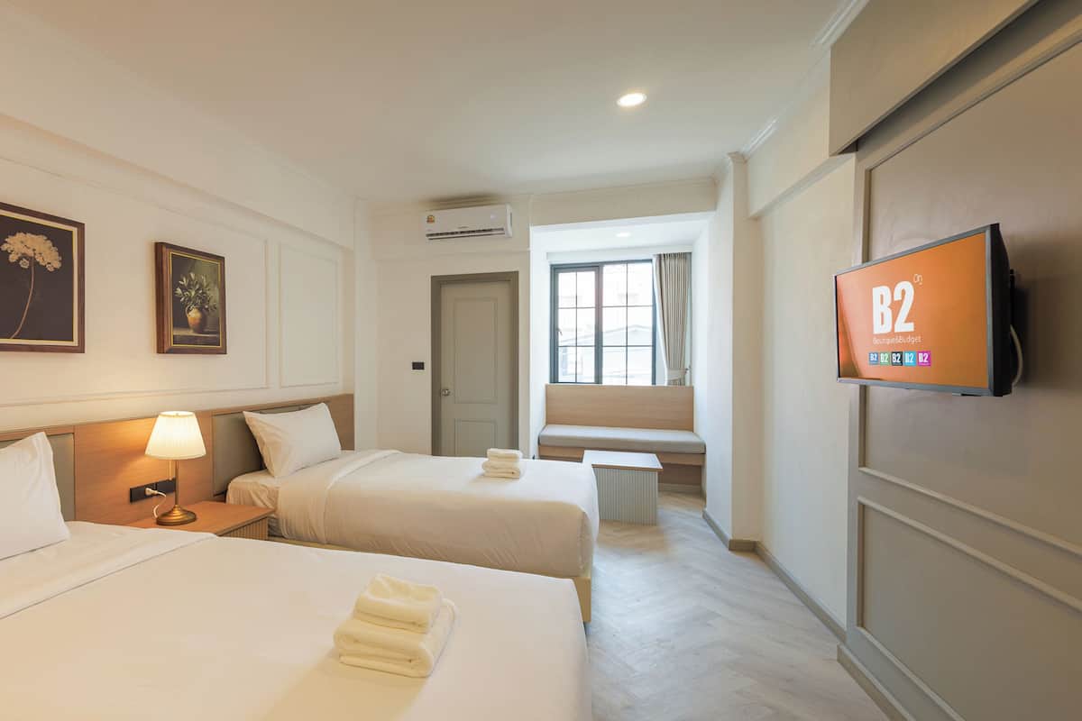 A hotel room with two beds, a TV, a window, and a door.