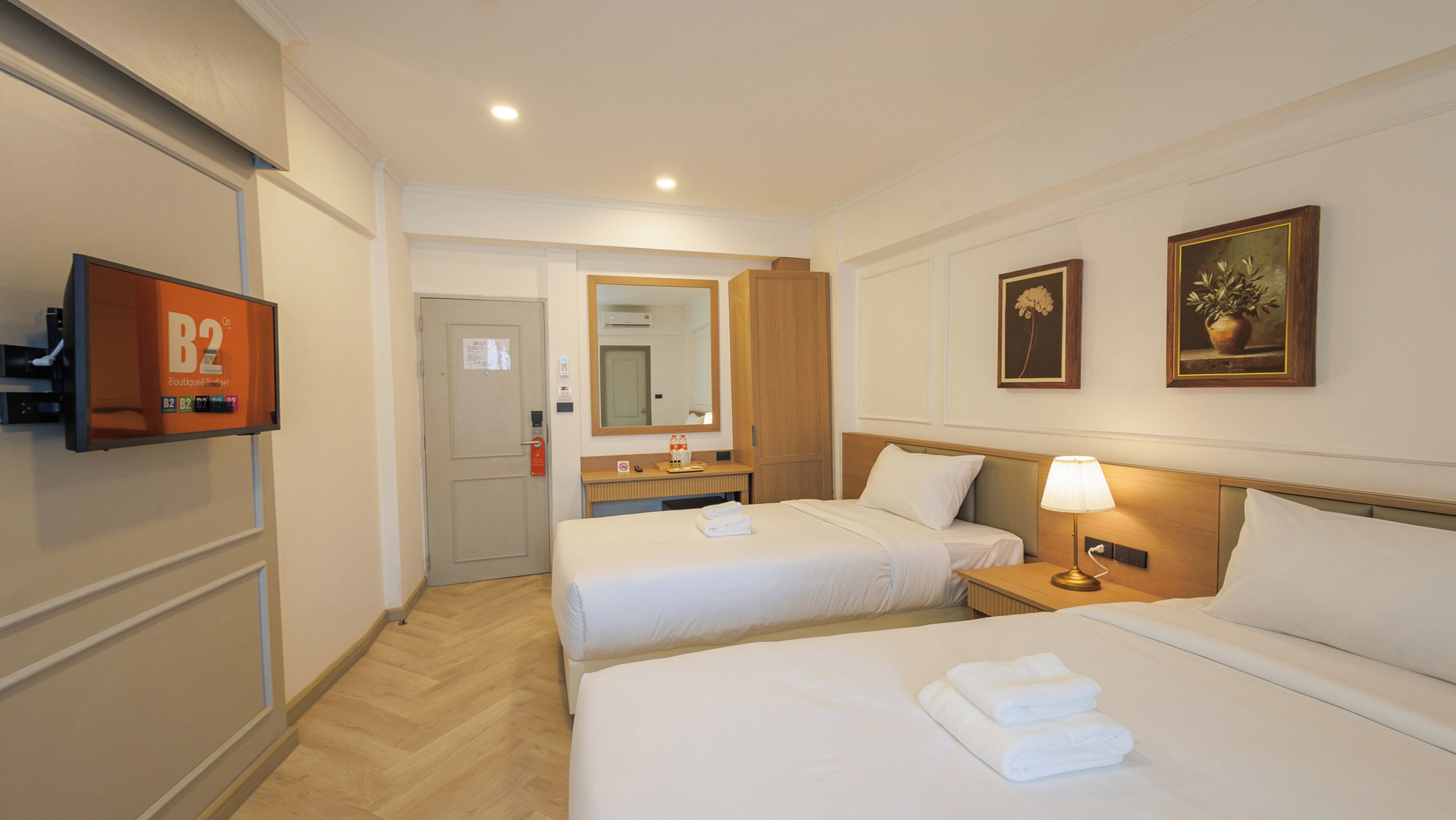 Habitació d'hotel amb dos llits, televisió, mirall i un quadre.