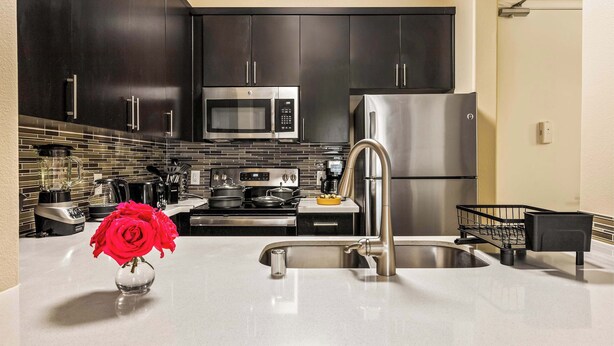 A modern kitchen with dark cabinets, stainless steel appliances, a sink, and a vase with red flowers. - Fable 2Bd-2Ba MarinaDelRey Parking, Pool & Jacuzzi (Marina del Rey)