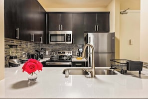 Una cocina moderna con armarios oscuros, electrodomésticos de acero inoxidable, un lavamanos y un florero con flores rojas.