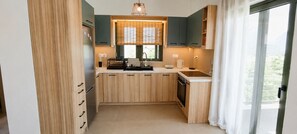 A compact kitchen with wooden cabinets, a built-in oven, and a window with blinds. - Panoramic Sea View Maisonette in Eretria | Private Family Retreat (Eretria)