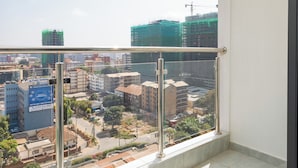 A balcony with a metal railing, a tiled floor, and a view of a cityscape with buildings and construction. - Stylish, fully equipped apartment in the prime area of Westlands, Nairobi (Nairobi)