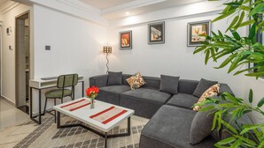 A modern living room with a grey sofa, a small table with a vase of flowers, and a desk with a chair. - Stylish, fully equipped apartment in the prime area of Westlands, Nairobi (Nairobi)