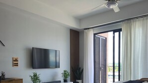 A modern bedroom with a bed, a TV mounted on the wall, a desk, and a potted plant.
