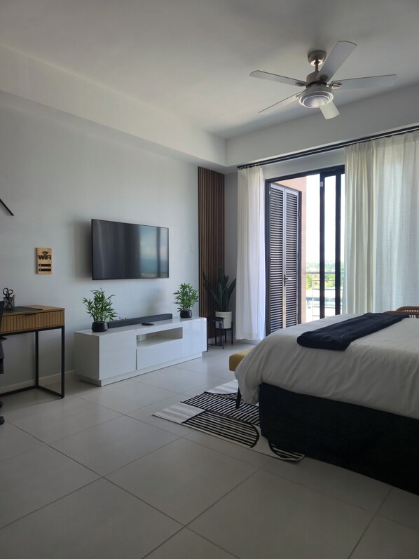 A modern bedroom with a bed, a TV mounted on the wall, a desk, and a potted plant.