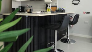 A modern kitchen with white cabinets, a black countertop, and a bar area with two black bar stools.