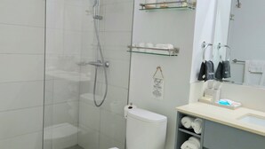 A modern bathroom with a glass shower enclosure, a toilet, a sink with a mirror, and neatly arranged towels.