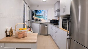 Eine moderne Küche mit Blick auf einen Strand durch ein Fenster, Edelstahlgeräte und eine Holzarbeitsplatte.