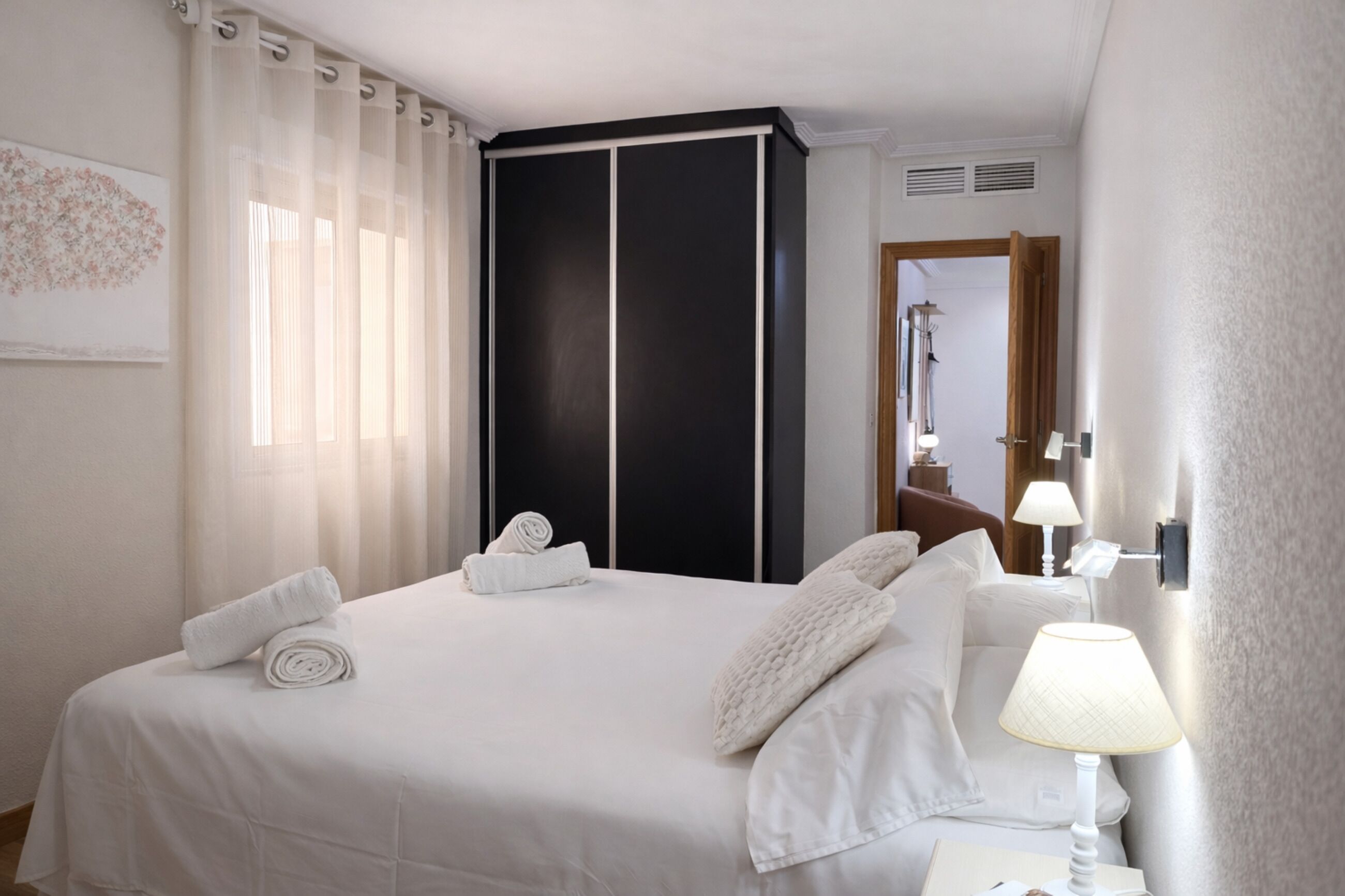 Une chambre d’hôtel avec un lit, une armoire, une table de chevet avec une lampe et une fenêtre avec des rideaux.