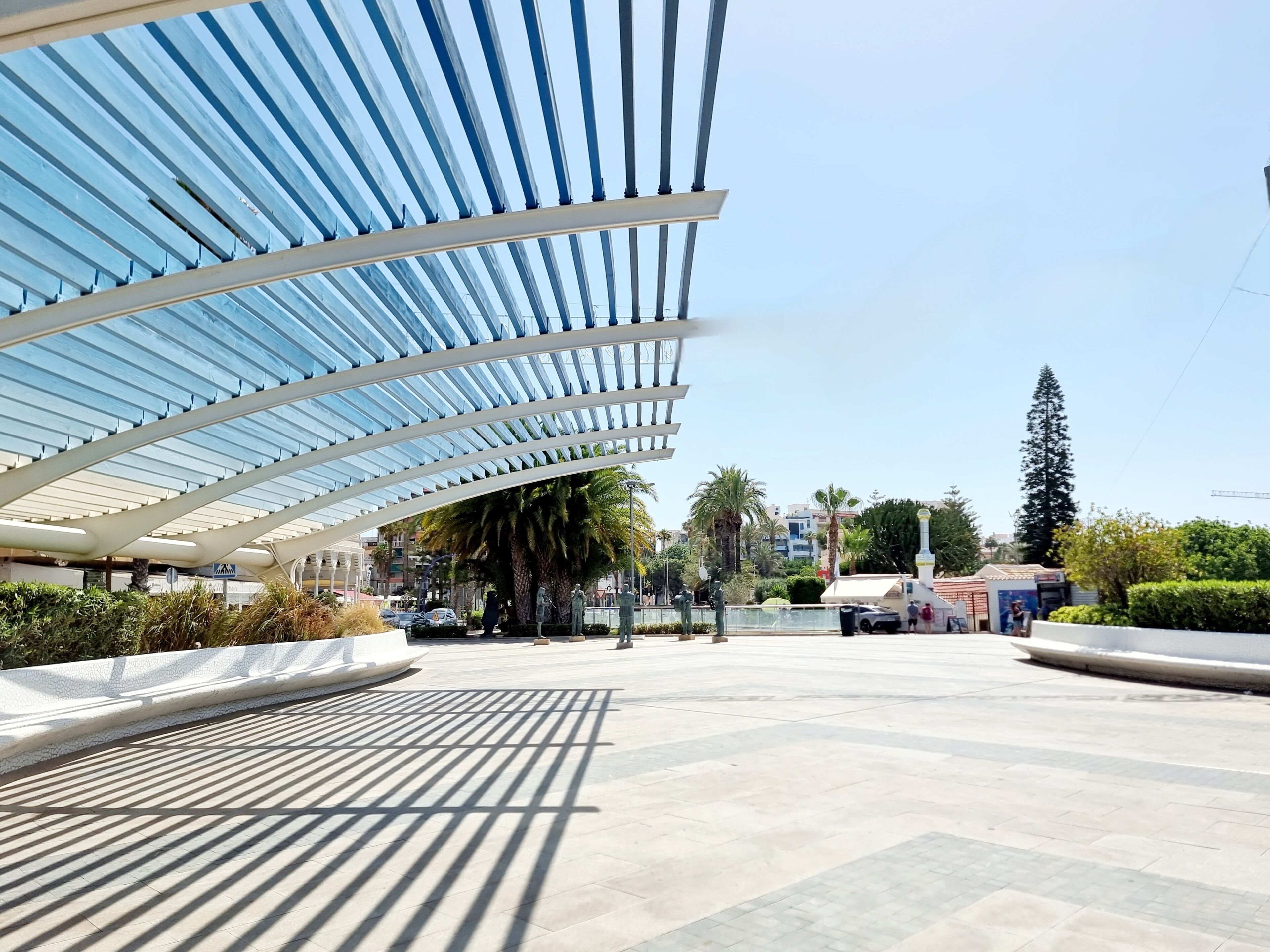 A covered outdoor area with a modern architectural design, featuring a patterned floor and a clear sky.