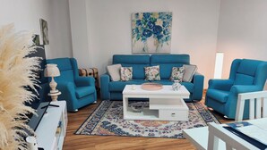 Ein Wohnzimmer mit blauem Sofagarnitur, einem weißen Couchtisch, einem gemusterten Teppich und einem Bild an der Wand.