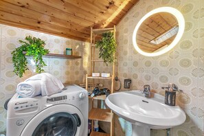 A laundry area with a washing machine, a shelf with plants, and a sink with a mirror. - La Mansarda Sul Lago: Rustic Attic Studio With Balcony & Parking (Nebbiuno)