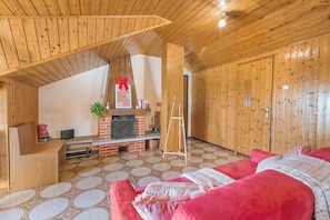 A cozy room with a wooden ceiling, a fireplace, a red sofa, and a tiled floor. - La Mansarda Sul Lago: Rustic Attic Studio With Balcony & Parking (Nebbiuno)
