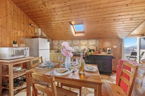 A wooden interior with a dining table set for four, a kitchen area, and a small skylight. - La Mansarda Sul Lago: Rustic Attic Studio With Balcony & Parking (Nebbiuno)