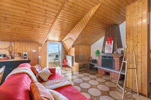 Una habitació acollidora amb sostre inclinat, un sofà vermell, una llar de foc i una televisió.