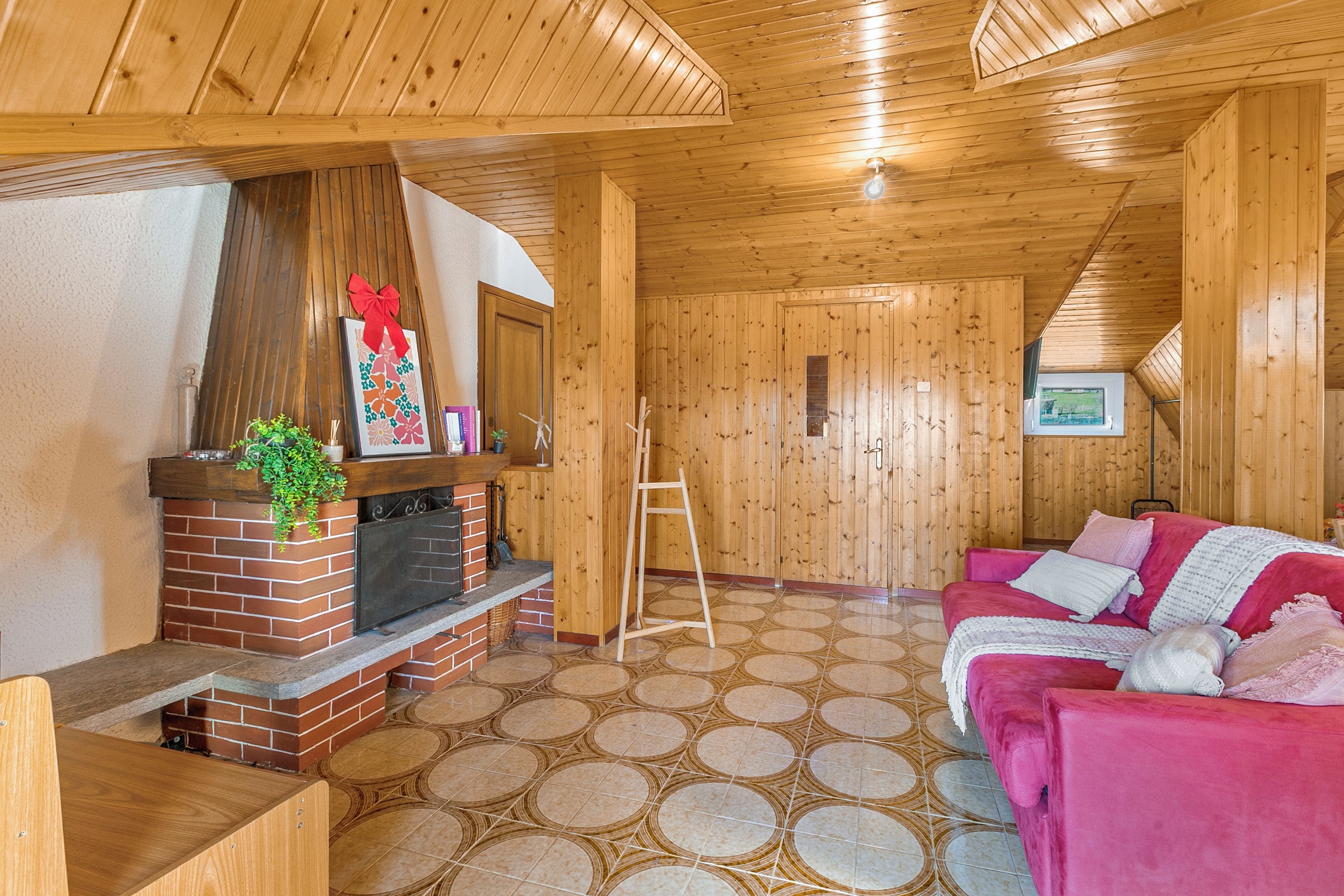 Un interior de madera con chimenea, un sofá rosa y un suelo estampado.