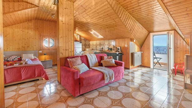 Interno di una baita in legno con zona pranzo, cucina e due camere da letto con letti.