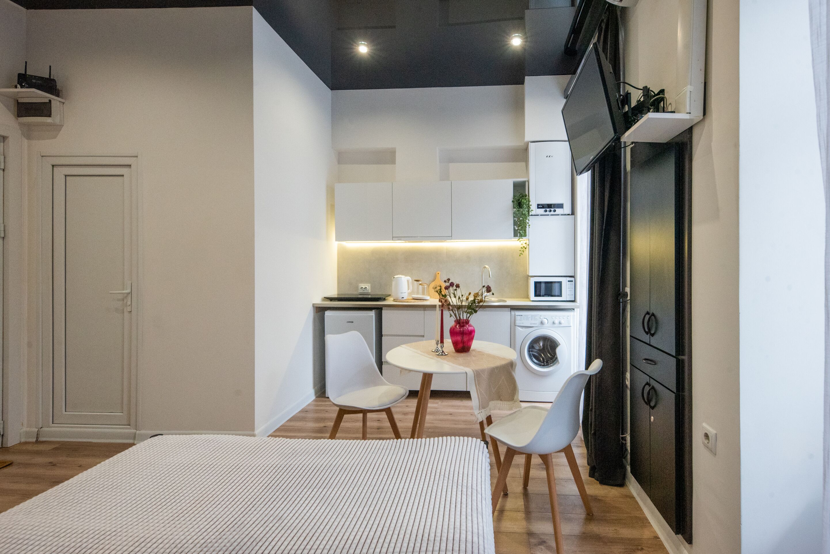 Un espacio habitable compacto con kitchenette, una zona de comedor con dos sillas, una mesita y una lavadora.