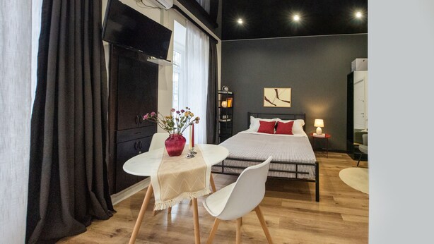 Quarto de hotel moderno com cama, mesa de cabeceira, luminária e área de jantar com mesa e cadeiras.