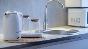 Uma cozinha com uma pia de aço inoxidável, uma chaleira branca e um micro-ondas.