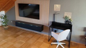 A modern living room with a large TV, a desk, a chair, and decorative wall art. - Vacation apartment Burgzauber (Burghausen)