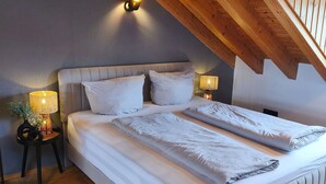 A bedroom with a sloped ceiling, a bed with white bedding, a nightstand with a lamp, and a small table with a plant. - Vacation apartment Burgzauber (Burghausen)