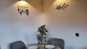 A dining area with a round table, six grey upholstered chairs, a vase with flowers, and wall-mounted lighting. - Vacation apartment Burgzauber (Burghausen)